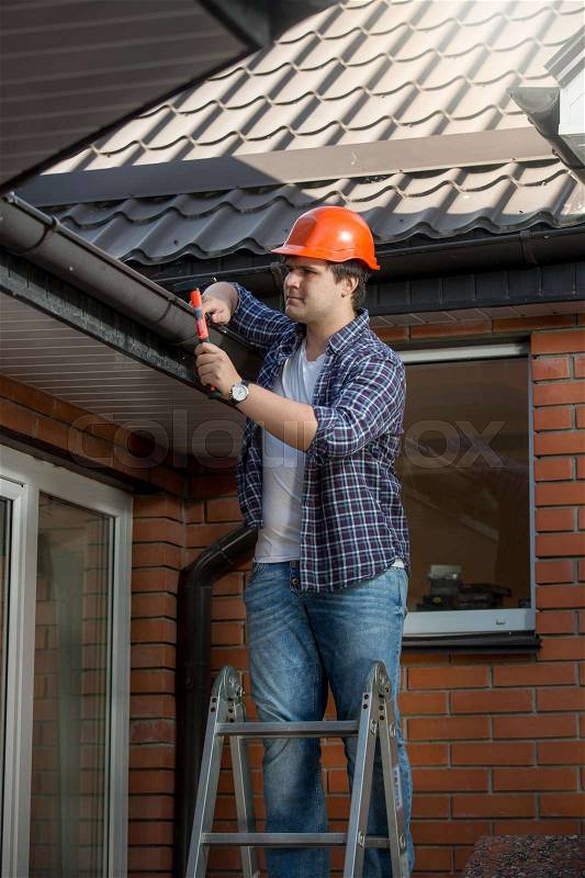 Smiling construction worker on step ladder under the house roof, stock photo