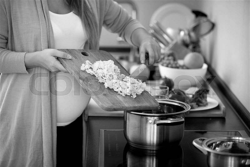 Closeup black and white photo of pregnant woman cooking vegetable soup, stock photo