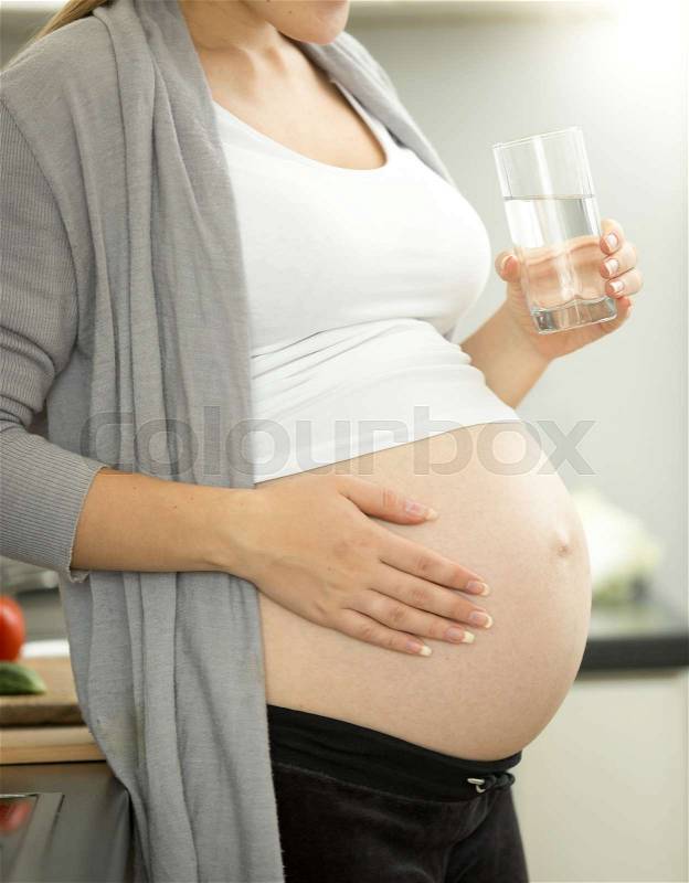 Pregnant woman on third trimester posing with glass of water on kitchen, stock photo