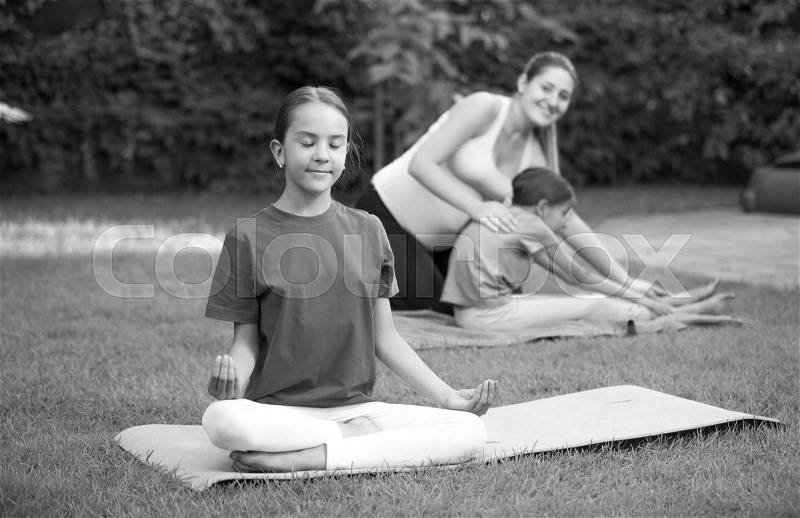 Black and white image of cute girl doing yoga during outdoor lesson at park, stock photo
