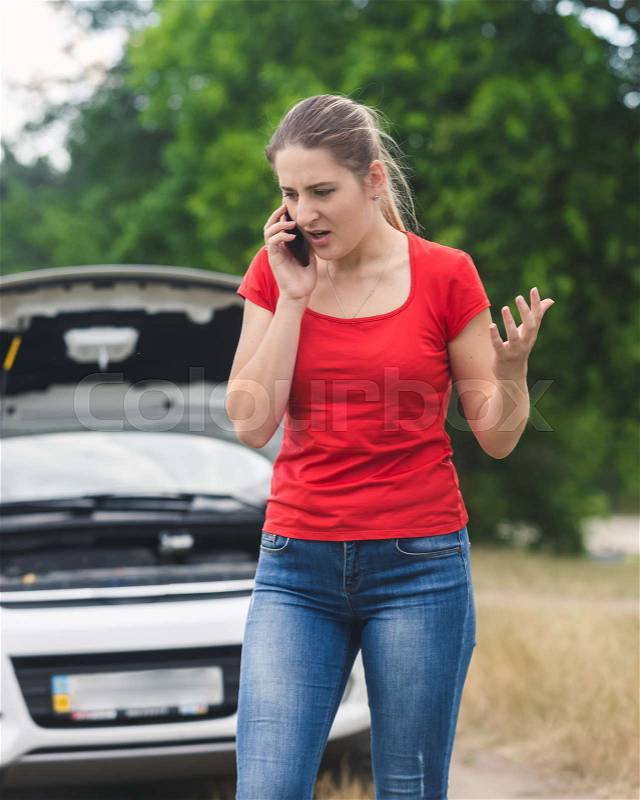 Angry young woman shouting in mobile phone because of the broken car, stock photo