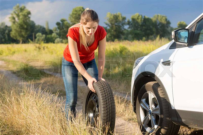Beautiful woman rolling spare tire to change the flat one, stock photo