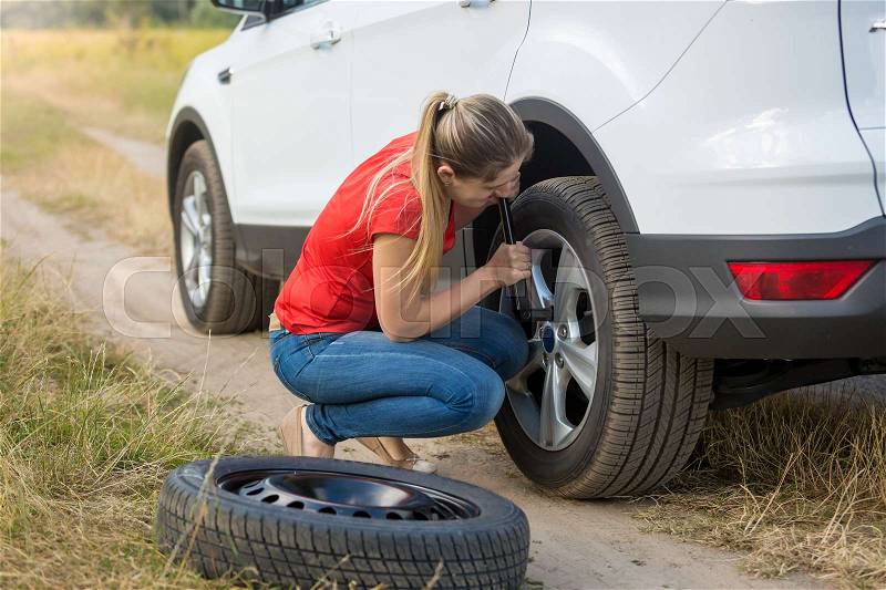 Young woman changing flat tire in field, stock photo