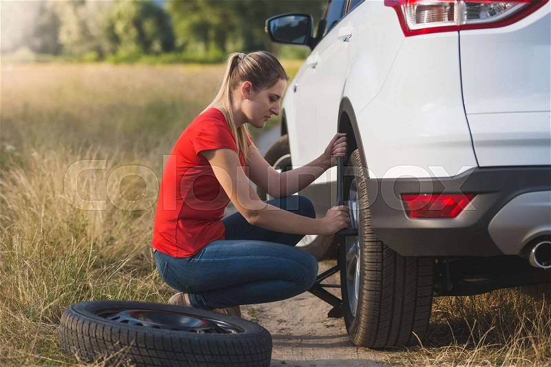 Young woman changing flat tire in field, stock photo