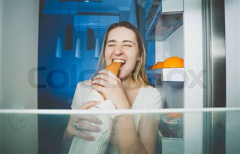 Portrait of young hungry woman eating bread at night, stock photo