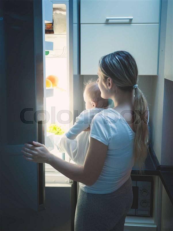 Mother with her baby opening refrigerator at late night, stock photo