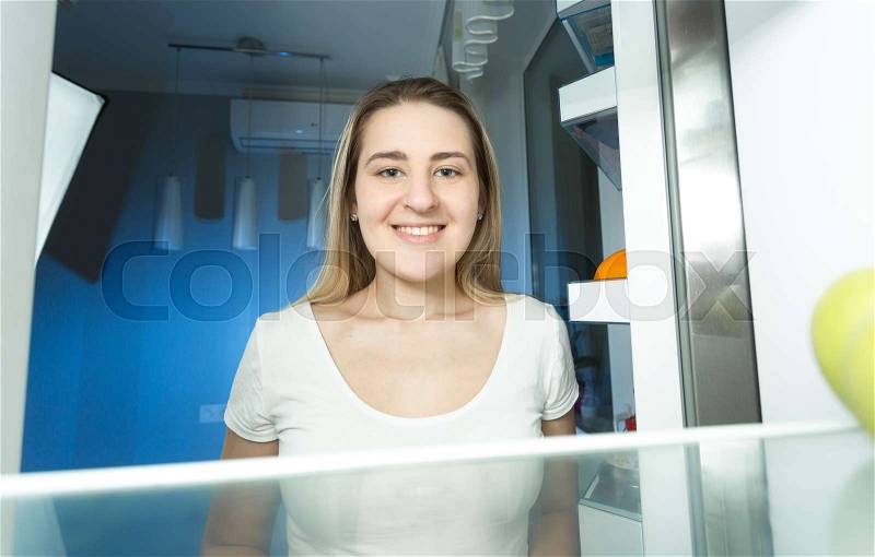 Portrait of beautiful woman in pajamas looking inside the refrigerator at night, stock photo