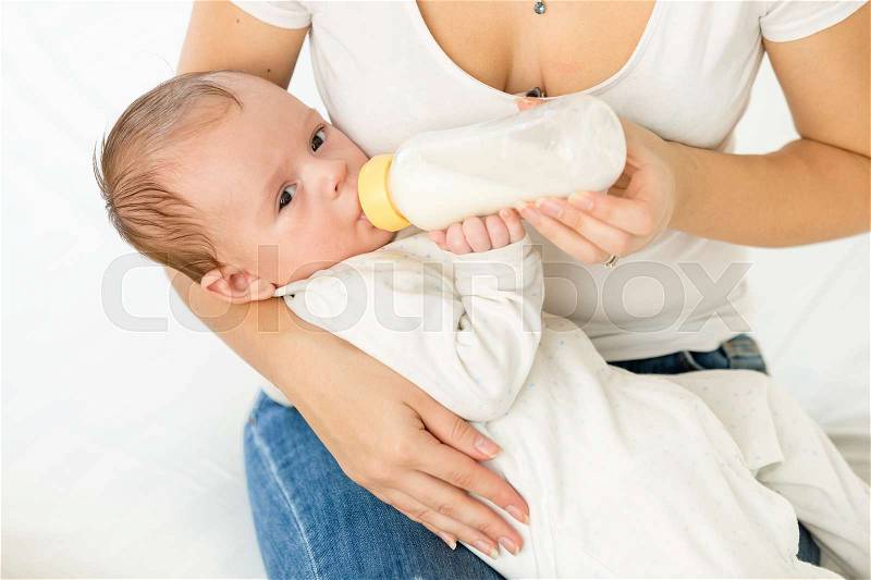 Portrait of young mother holding her baby and feeding with milk from bottle, stock photo