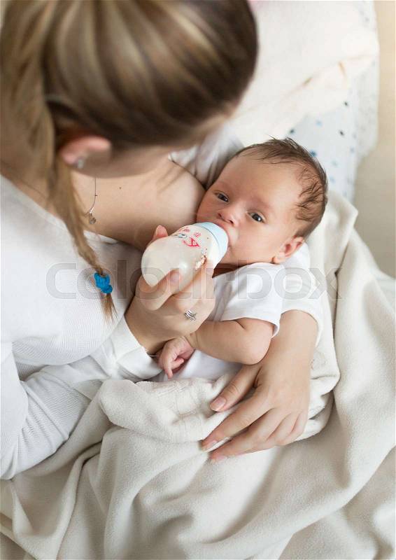 Closeup portrait of young mother feeding baby with milk from bottle, stock photo