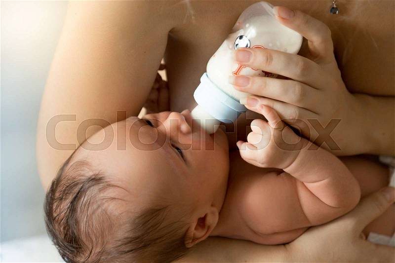 Closeup portrait of mother feeding newborn baby from bottle, stock photo