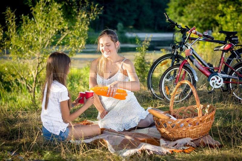 Smiling woman sitting on blanket under big tree with her daughter, stock photo
