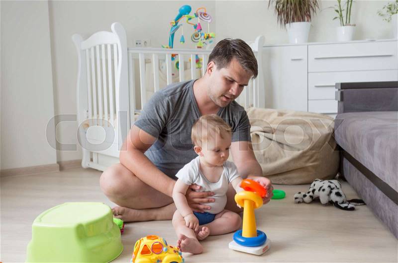 Father sitting on floor with his baby and playing with toys, stock photo