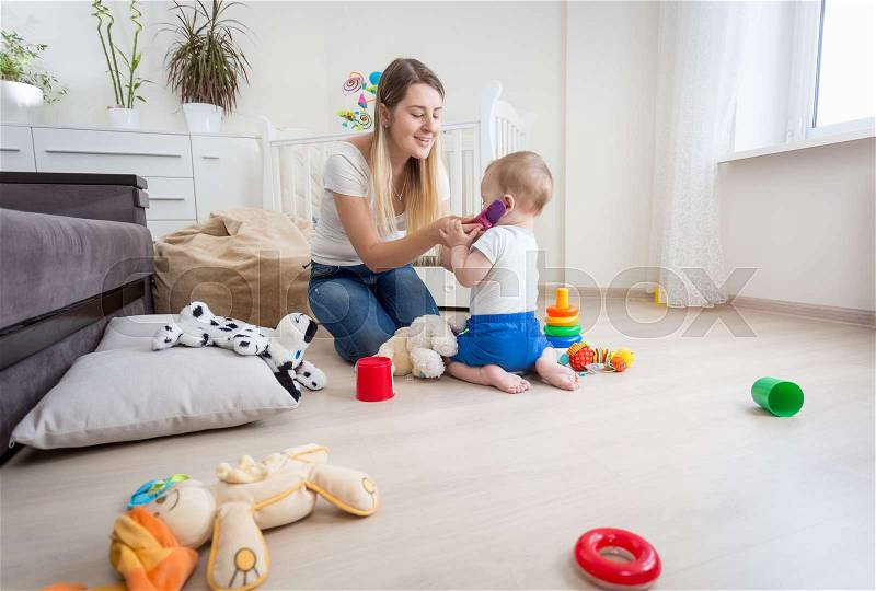 Young mother playing her baby son and pretending talking by phone, stock photo