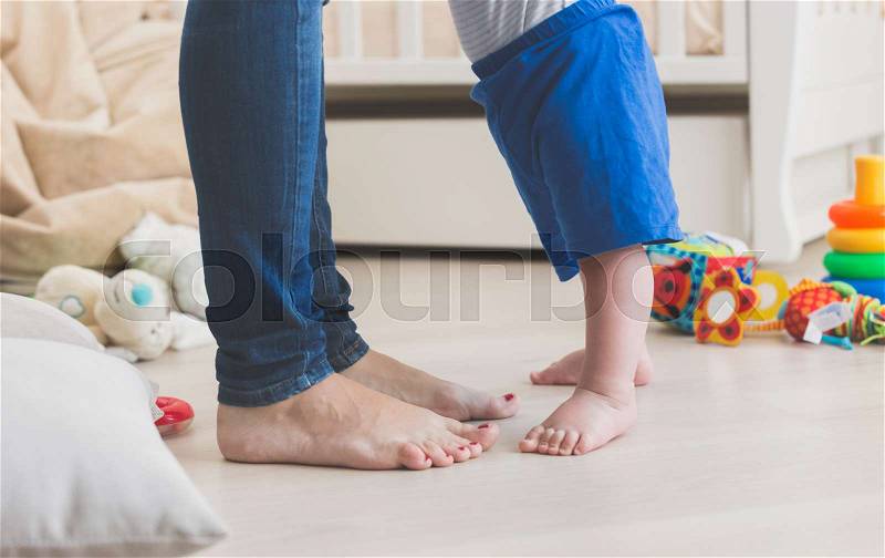 Closeup of small baby\'s feet on floor next to mothers feet, stock photo