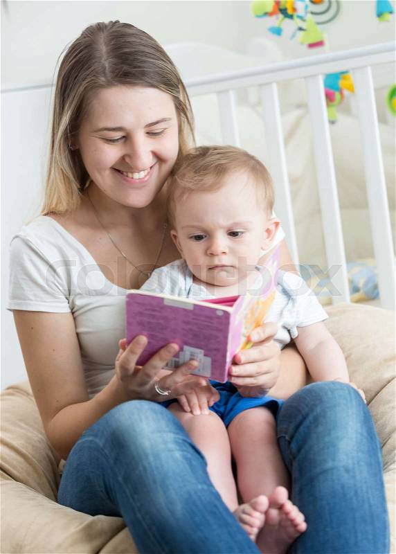 Beautiful cheerful mother reading book with her baby boy, stock photo