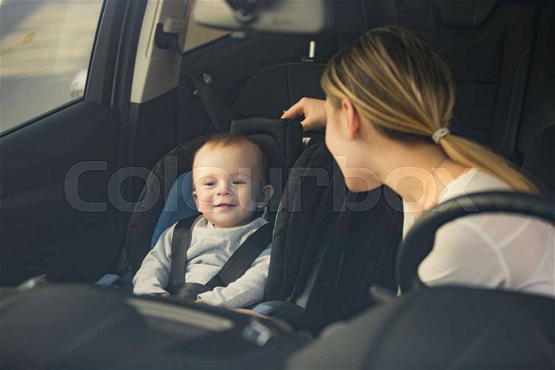 Portrait of mother looking at baby sitting on car front seat, stock photo