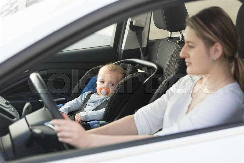 Woman driving car with baby sitting on front seat, stock photo