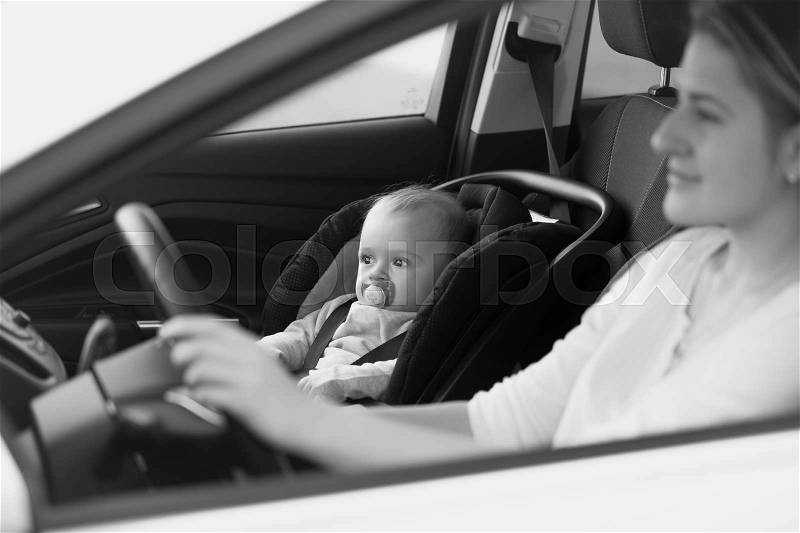 Black and white portrait of mother driving car with her baby sitting on front seat, stock photo