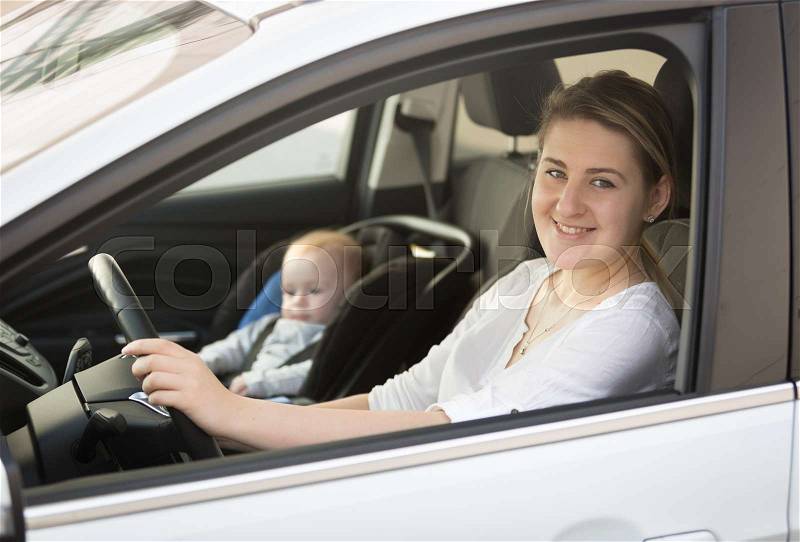 Portrait of mother driving car with little baby boy sitting in safety seat, stock photo