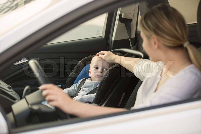 Young smiling woman posing in car with her baby boy, stock photo
