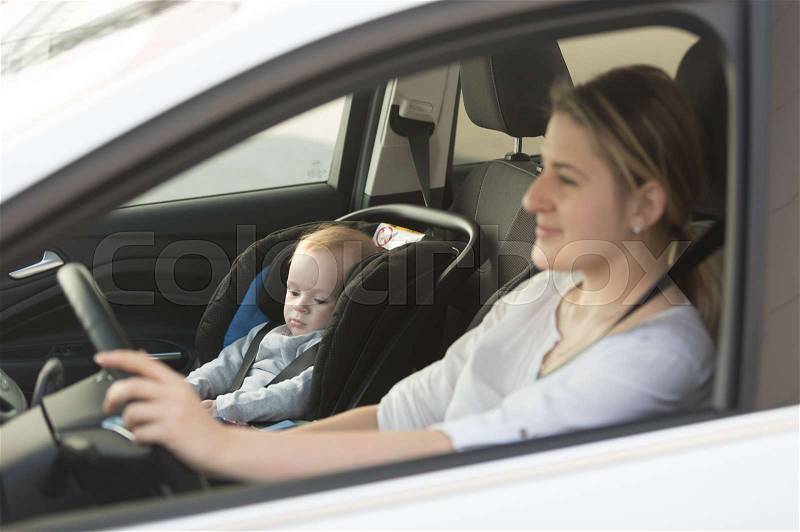 Young mother driving car with her baby boy sitting in car in baby seat, stock photo