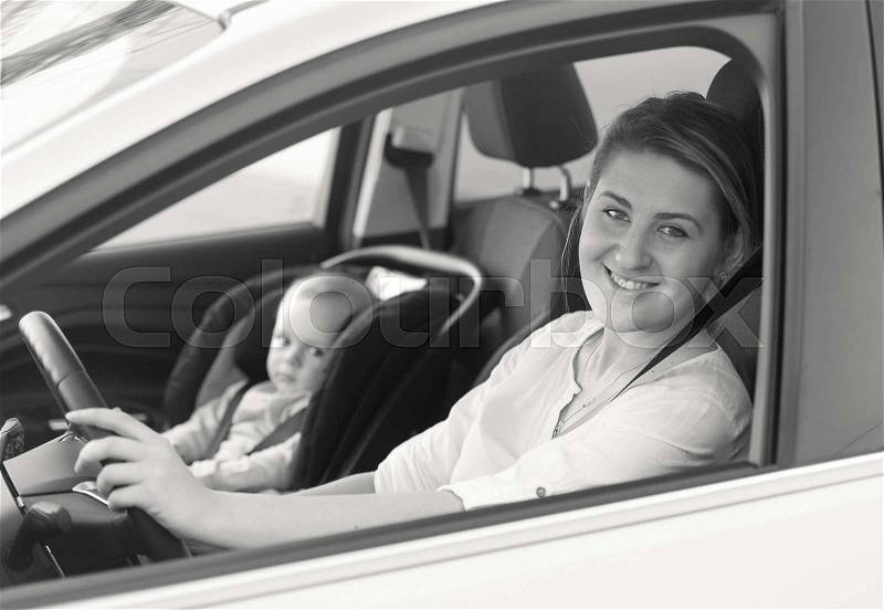 Black and white portrait of young mother driving car with her little baby on front seat, stock photo