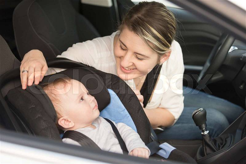 Smiling mother in car having her baby boy in safety seat, stock photo