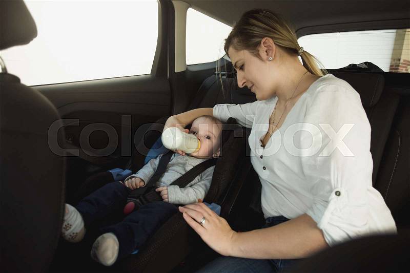 Portrait of smiling young mother feeding baby boy in car, stock photo