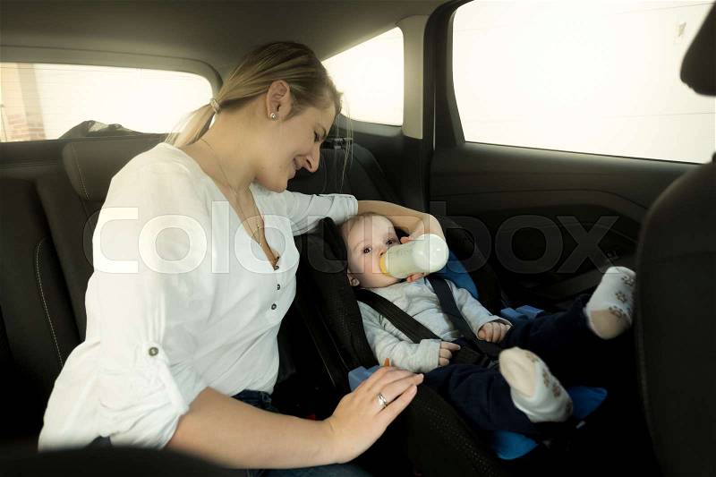 Portrait of mother feeding baby in car safety seat, stock photo
