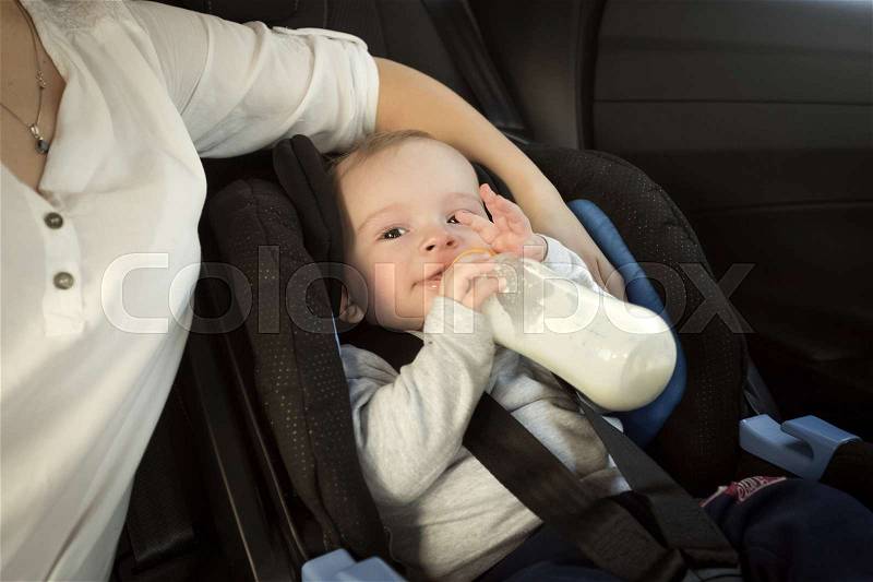 Portrait of mother feeding baby in car from bottle, stock photo