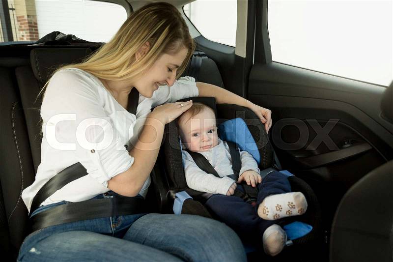 Portrait of caring mother with baby boy on car back seat, stock photo