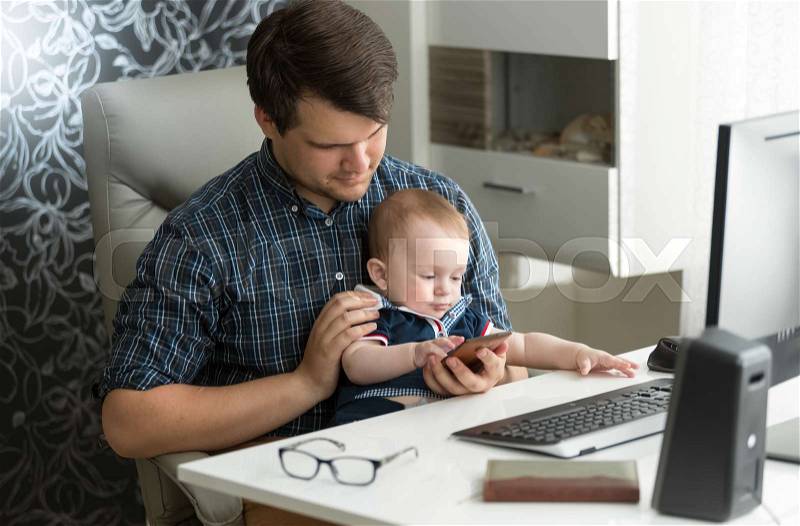 Young father working at computer playing with his baby son, stock photo