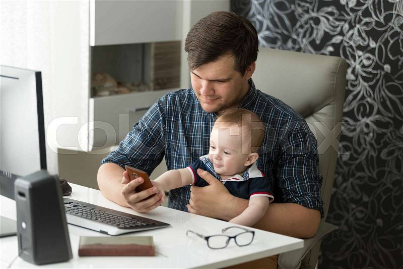 Young father working in office and taking care of baby son, stock photo