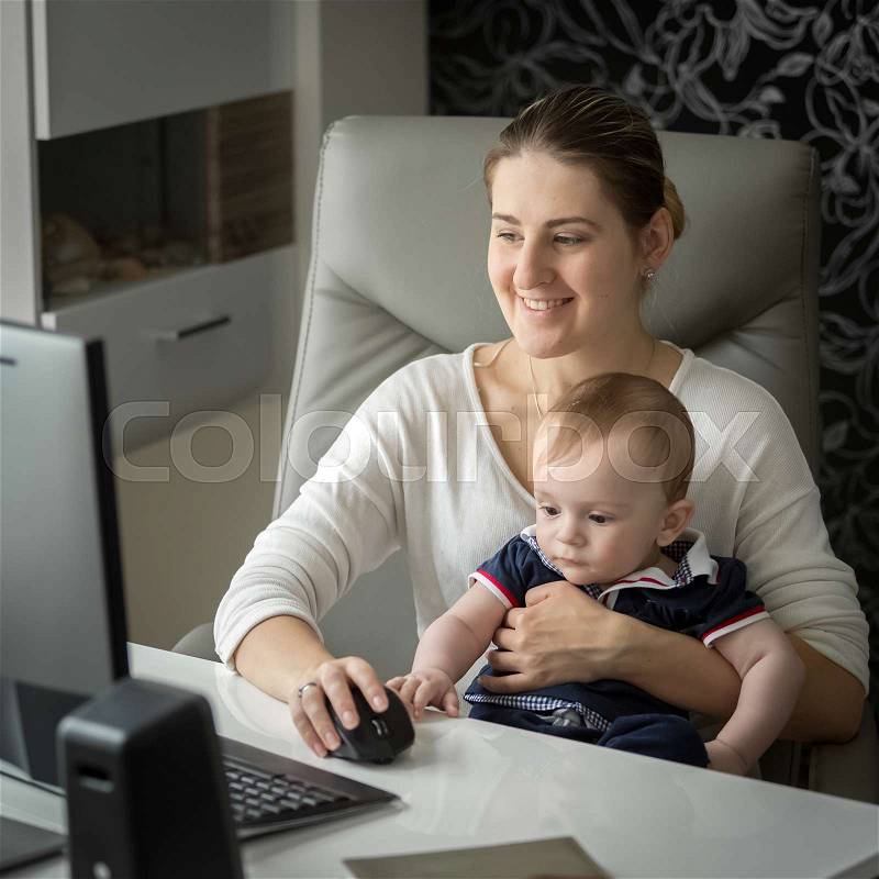 Woman working at home at computer and taking care of her baby, stock photo