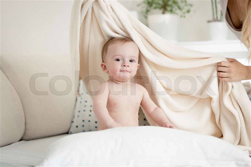 Mother covering her baby boy in big white blanket on bed, stock photo