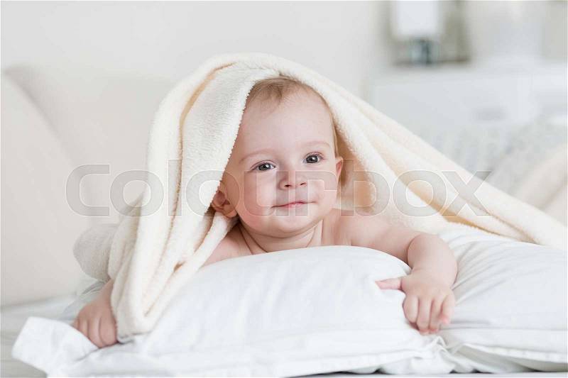 Cute baby boy lying under white blanket on bed, stock photo