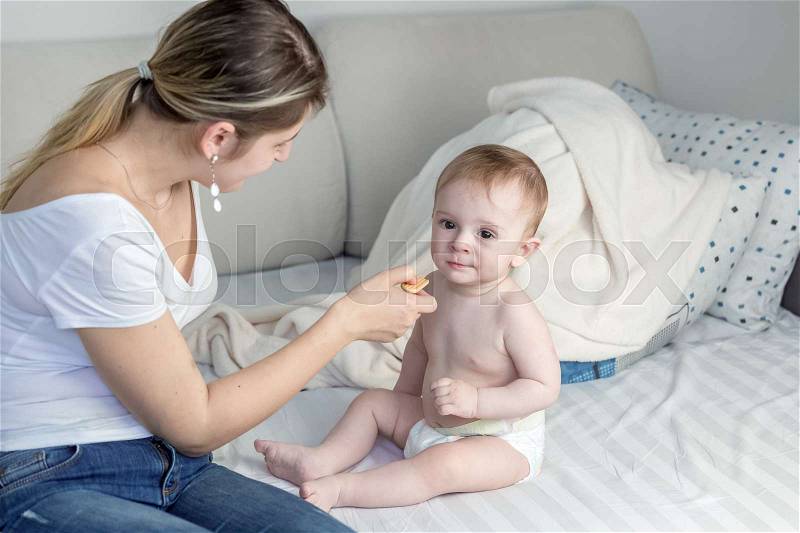Parent giving biscuit for babies to 9 months old son at bedroom, stock photo