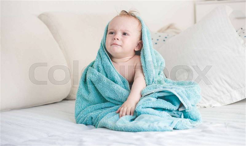 Adorable baby boy after shower covered in blue blanket on sofa, stock photo