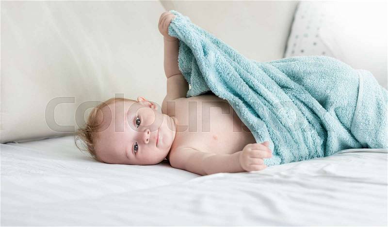 9 months old baby boy sitting on bed under towel, stock photo