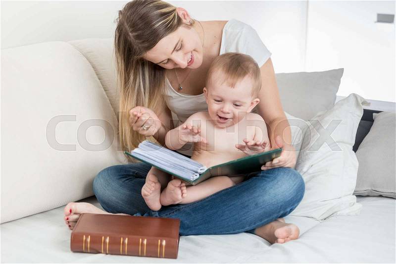 Happy smiling mother looking at photo album with her baby boy, stock photo