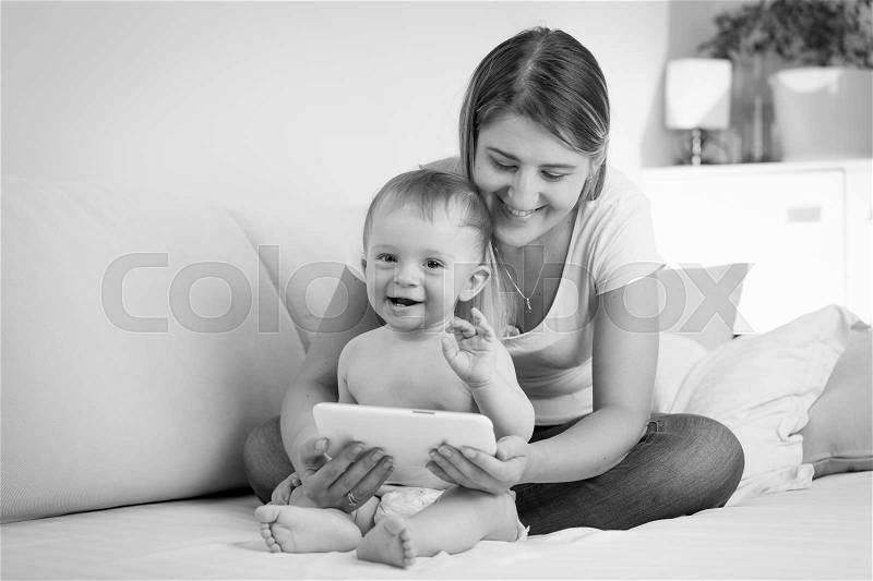 Black and white image of happy cheerful baby boy playing on tablet PC with mother, stock photo