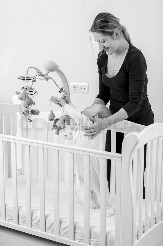 Black and whit eimage of young smiling mother standing at cot with her baby boy, stock photo