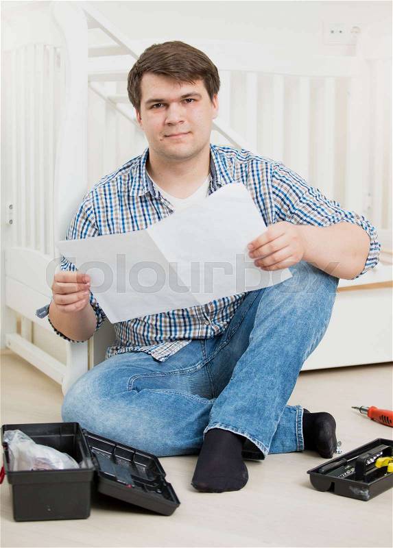 Puzzled man reading assembly instructions to baby's cot, stock photo