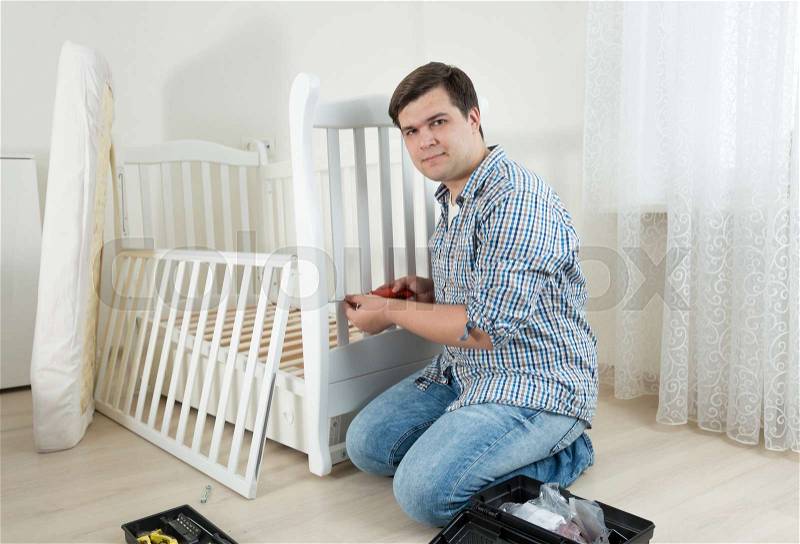 Handyman sitting on floor at empty room and assembling new furniture, stock photo