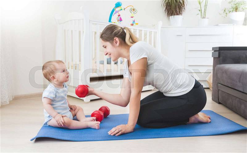 Smiling mother doing physical exercise with her baby on floor at living room, stock photo