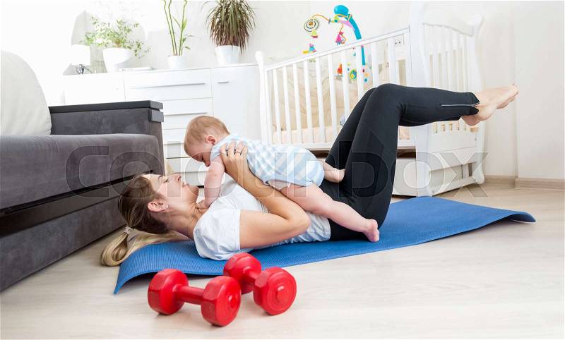 Happy mother doing exercise at home and having fun with her baby boy, stock photo