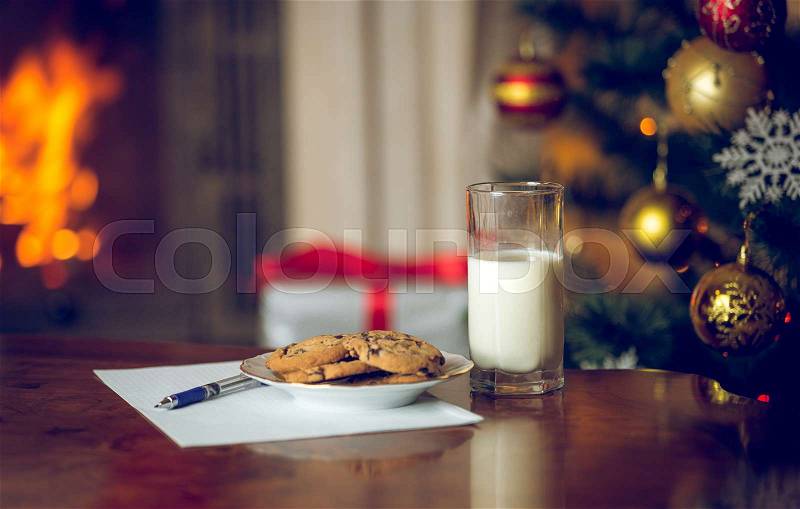 Closeup image of treats and letter to Santa on wooden table next Christmas tree, stock photo