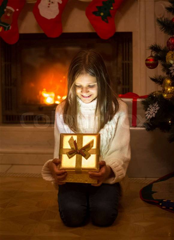 Cheerful girl opening box with Christmas present. Light and shiny sparkles going out of the box, stock photo