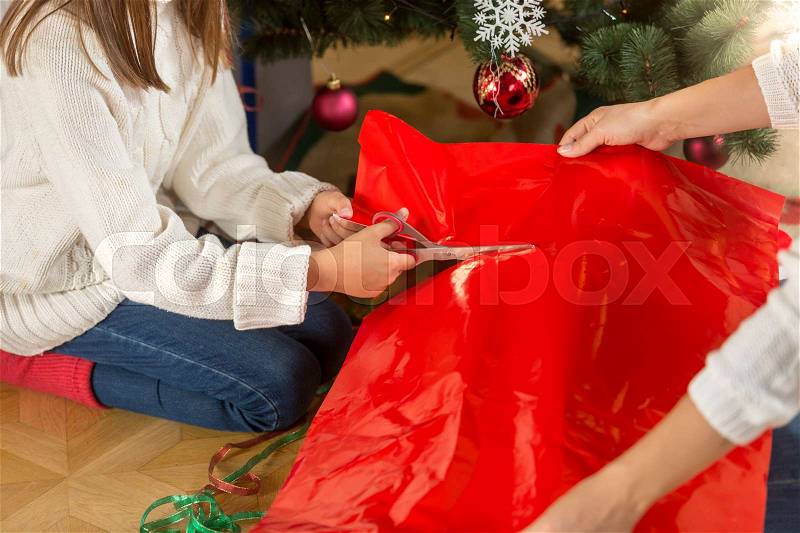 Cute girl cutting red paper for wrapping Christmas presents, stock photo