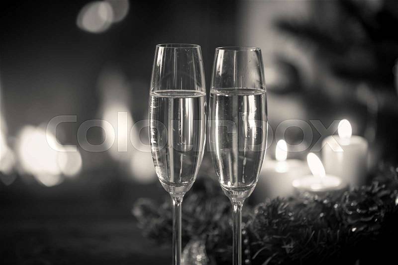 Closeup black and white image of two glasses of champagne in front of Christmas wreath and burning fireplace, stock photo